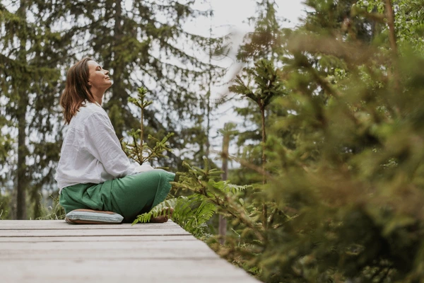 Person sitting quietly outdoors with eyes closed, focusing on natural breathing